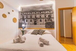 A hotel room with a bed, a nightstand, a lamp, and a wall mural of a building. - Editar Intimate retreat with Andalusian essence 3 (Úbeda)