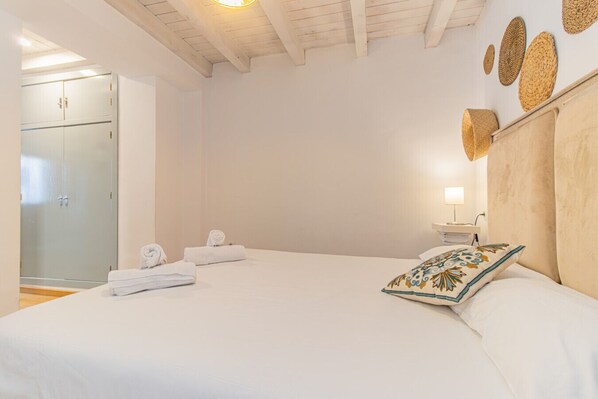 A bedroom with a large bed, a wooden headboard, a bedside table with a lamp, and a wardrobe.