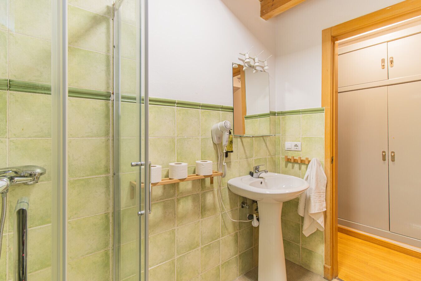 A bathroom with a glass shower enclosure, a sink with a mirror, and a wooden cabinet.