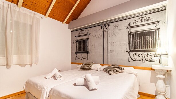 Un dormitorio con una cama grande, ropa de cama blanca, techo de madera y una pared con detalles decorativos.