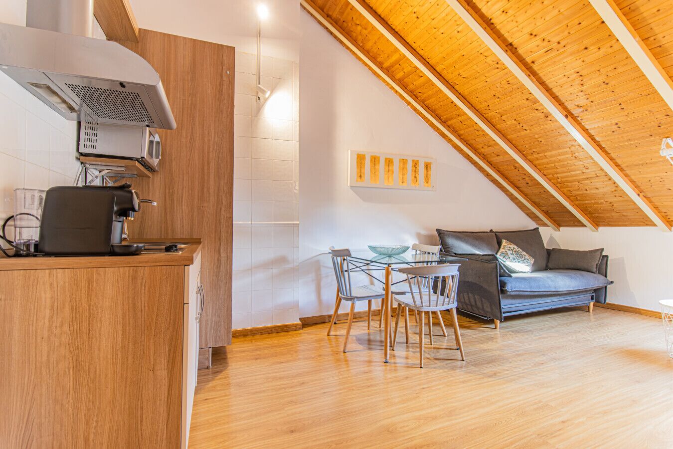 Een moderne keuken met een ingebouwde espressomachine, een eethoek met een glazen tafel en stoelen, en een slaapkamer op een entresol met een schuine hemel.