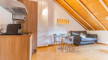 Een moderne keuken met een ingebouwde espressomachine, een eethoek met een glazen tafel en stoelen, en een slaapkamer op een entresol met een schuine hemel.