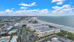 Un paisaje urbano costero con un complejo hotelero en primera línea de playa, que incluye varios edificios, un aparcamiento y una carretera que conduce a la playa.
