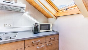 Une cuisine compacte équipée d’un four à micro-ondes encastré, d’une machine à café et de meubles de rangement en bois.