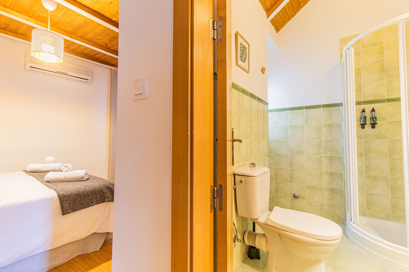 A room with a bed, a bathroom with a toilet and shower, and an air conditioning unit.