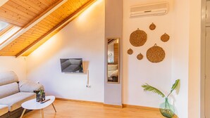Un salon chaleureux avec un plafond en pente, un téléviseur à écran plat fixé au mur, un canapé, une petite table basse et un élément décoratif mural.