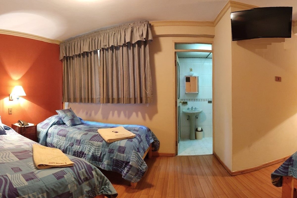 Une chambre d’hôtel avec deux lits, une télévision, une salle de bain visible à travers une porte ouverte et un téléphone sur la table de chevet.