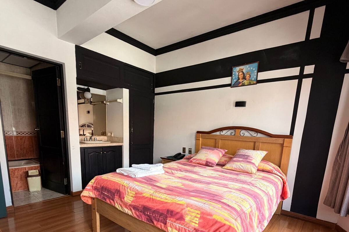 Une chambre à coucher avec un lit en bois, une salle de bain avec un miroir et un luminaire au plafond.
