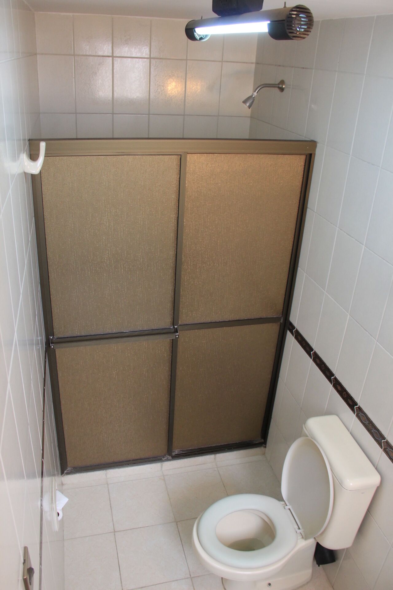 Ein kleines Badezimmer mit Toilette, Duschkabine und einer Leuchte über der Dusche.