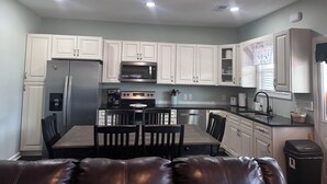 A modern kitchen with white cabinets, stainless steel appliances, a dining table with chairs, and a black trash bin.