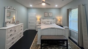 A bedroom with a bed, a dresser, a bench, a ceiling fan, and a window with blinds.