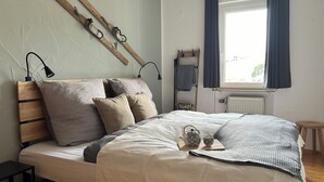 A neatly made bed with a headboard, a bedside table, a window with curtains, and a radiator. - Vacation apartment "SchwarzwaldnACHT" - peace & nature in Todtnauberg - Mein SWH (Todtnauberg)