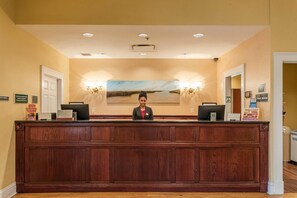 A reception desk with a wooden finish, two computer monitors, and a framed landscape painting above.