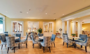 A spacious dining area with round tables and chairs, large windows, and a warm color scheme.