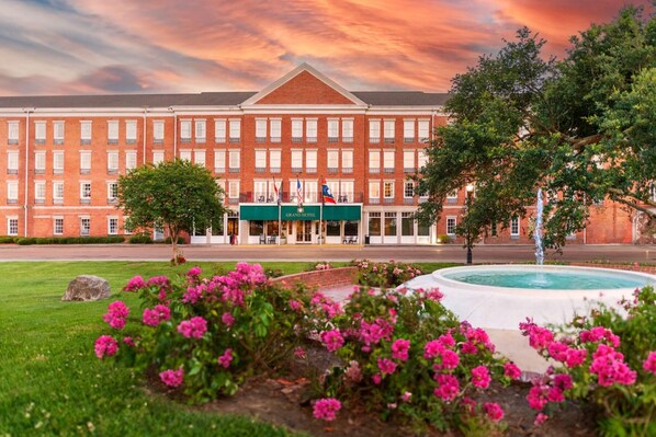 A large brick building with a green awning and a fountain in the foreground.