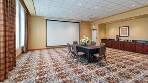 Una sala conferenze con pavimento in moquette, uno schermo per proiettore, un tavolo con sedie e un angolo cottura.