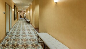 Un corridoio d'hotel con tappeto a motivi, panche e luci a parete.