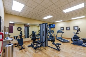 A gym with various exercise equipment, a clock, and a television on the wall.