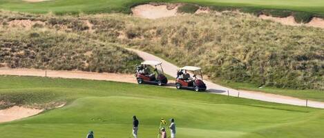 Golfkenttä, jossa on hiekkabunkkereita, vesialue ja golfauto.