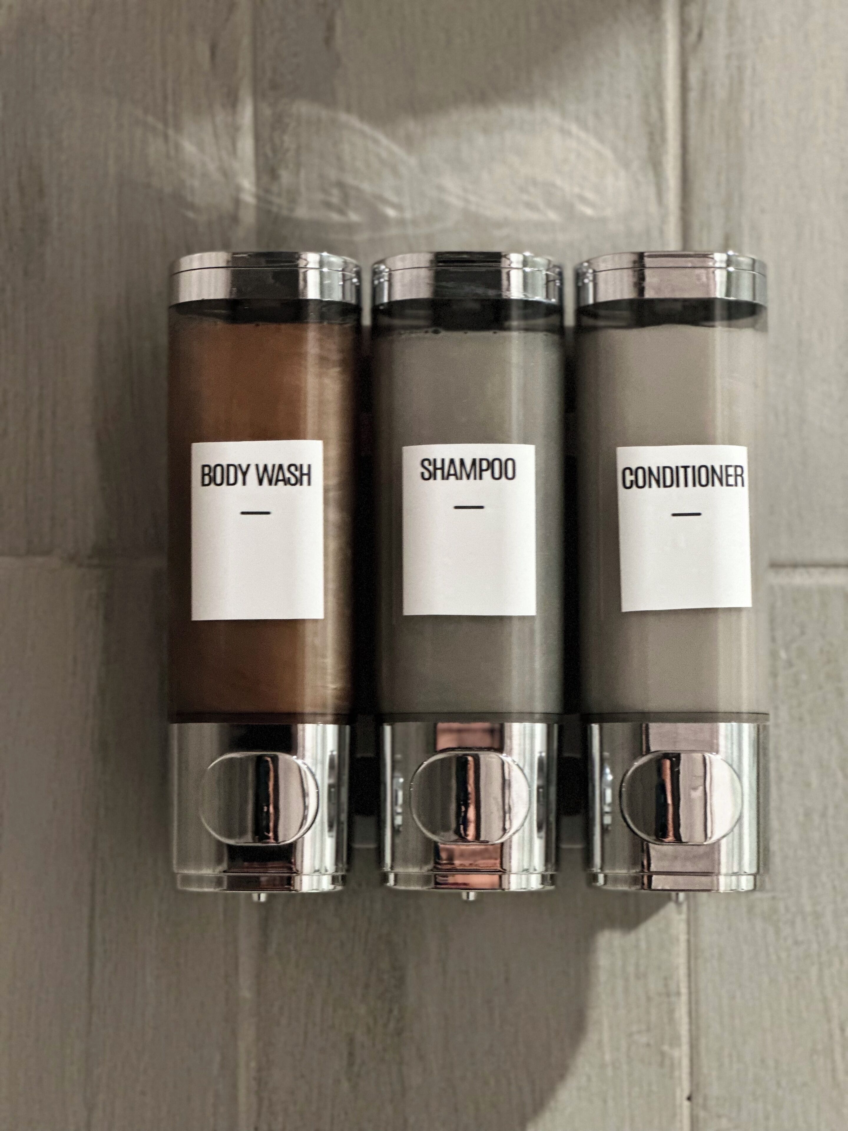 Drei zylindrische Behälter mit den Aufschriften Duschgel, Shampoo und Spülung.