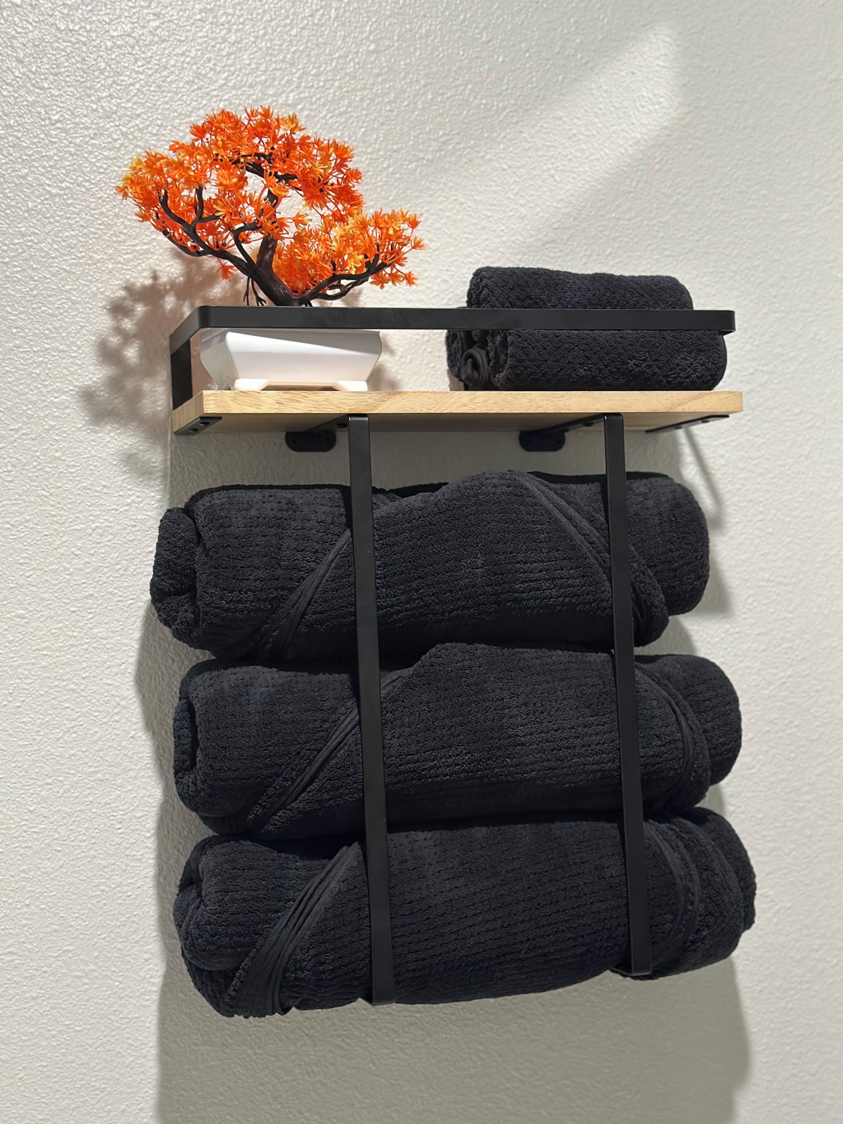 A wall-mounted towel rack with four folded towels and a small potted plant.