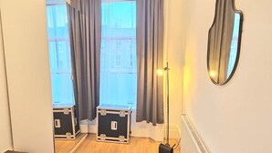 Une chambre d’hôtel avec une grande fenêtre, un miroir, un radiateur et une valise posée sur le sol.