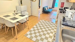 Une cuisine de taille réduite, dotée d’un évier, d’un coin repas avec une table et des chaises, et d’un tapis à carreaux sur le sol.