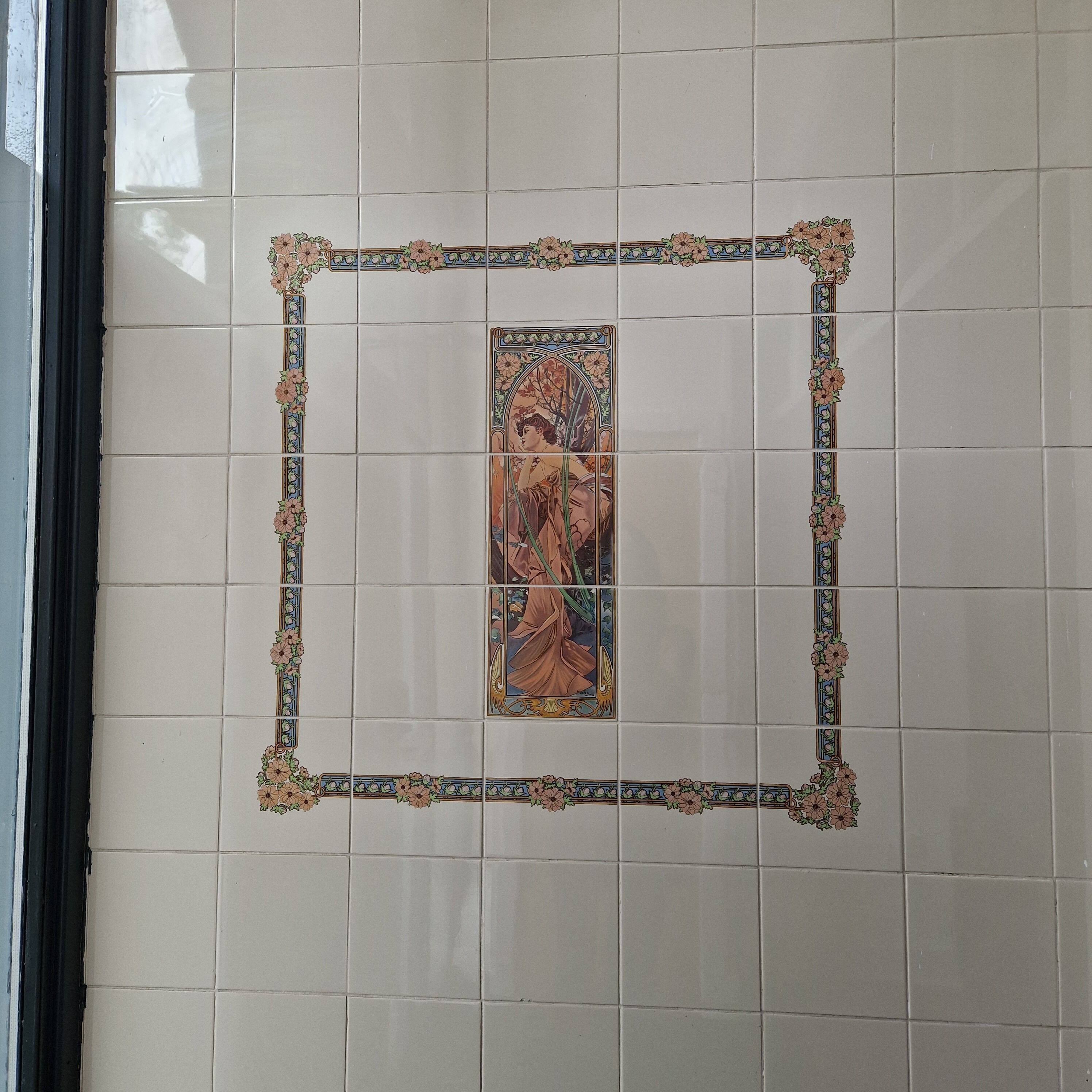 A tiled wall with a central framed artwork depicting a figure in a landscape.