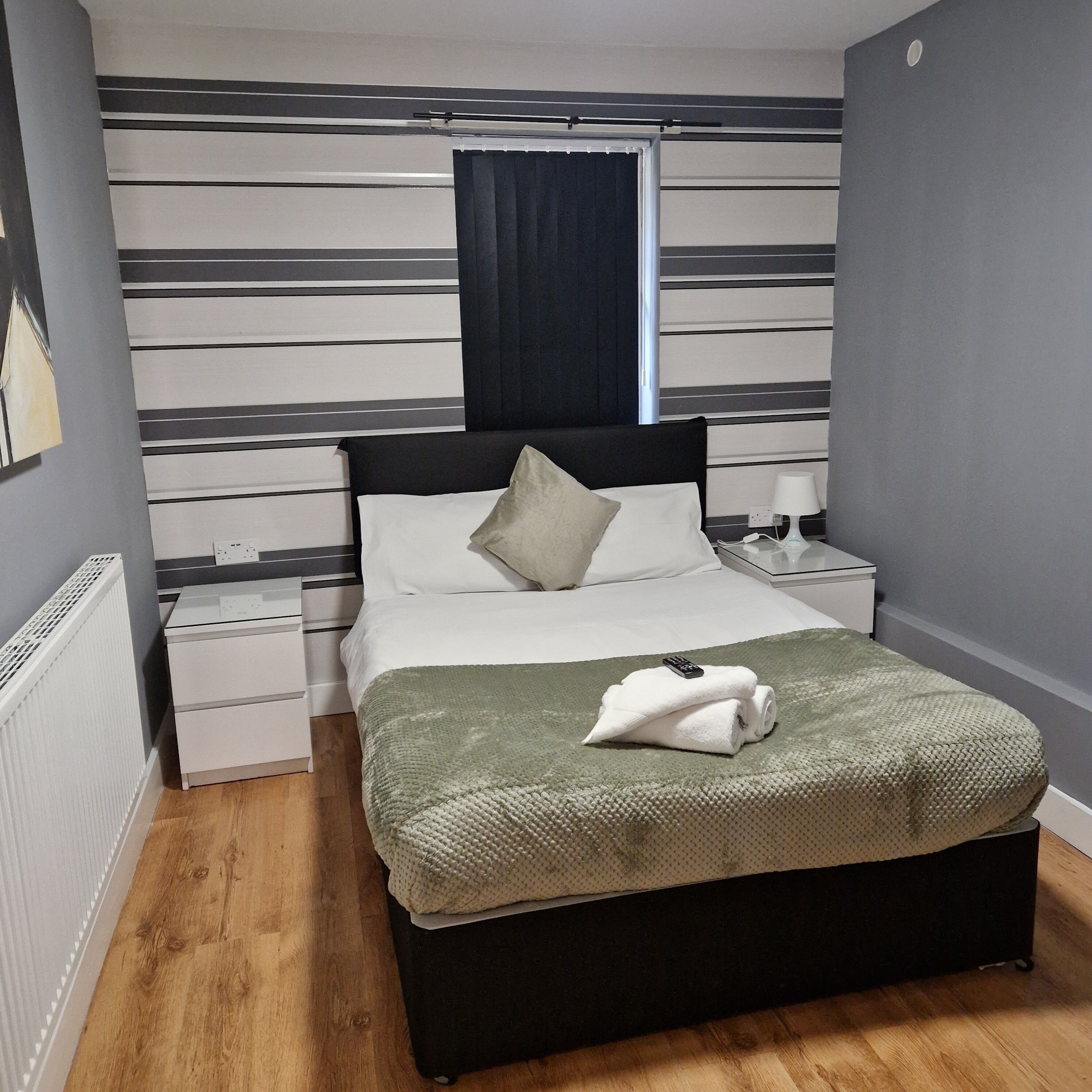 Un dormitorio ordenado con cama, mesitas de noche, lámpara y ventana con cortinas.