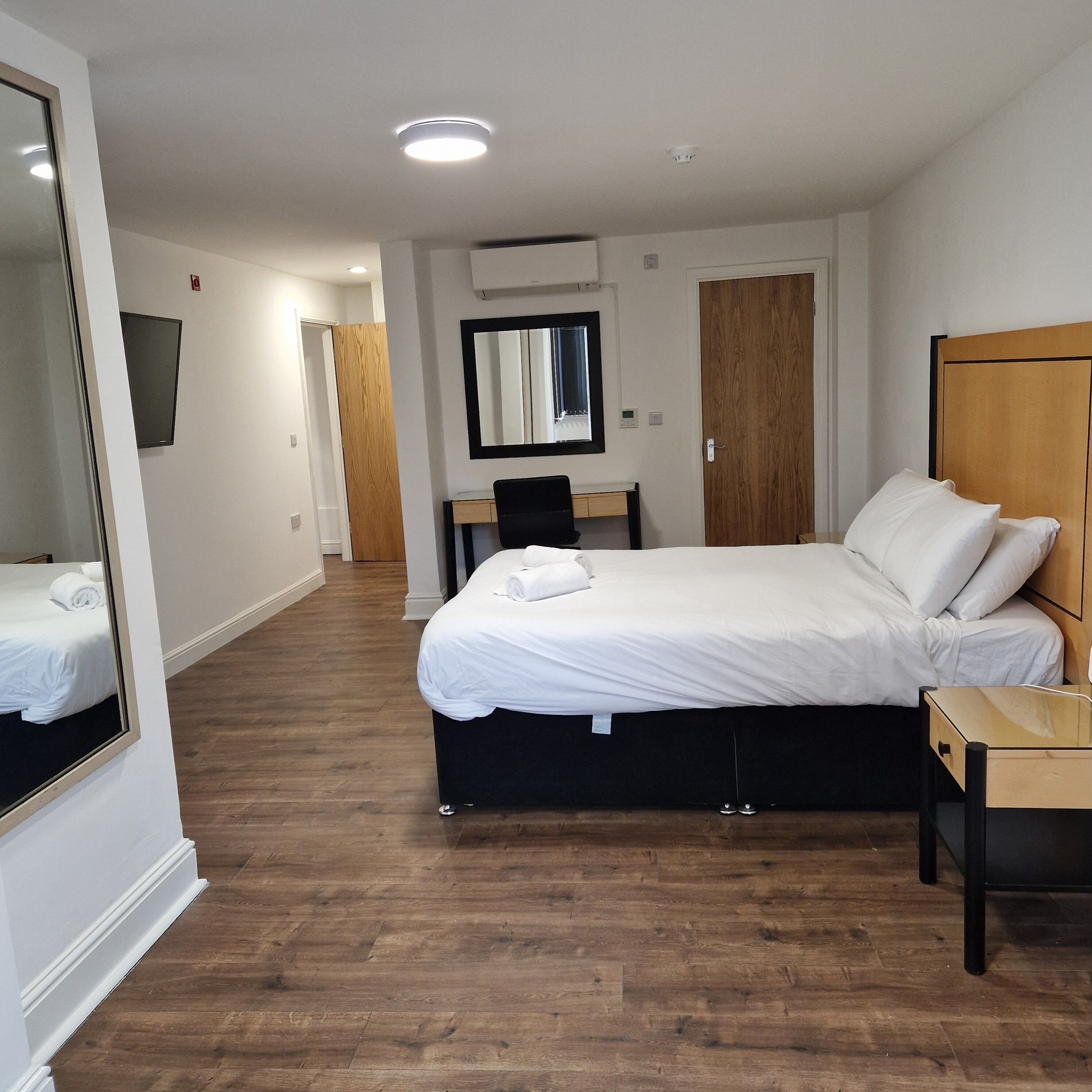 A hotel room with a bed, a desk, a chair, a mirror, and a wardrobe.