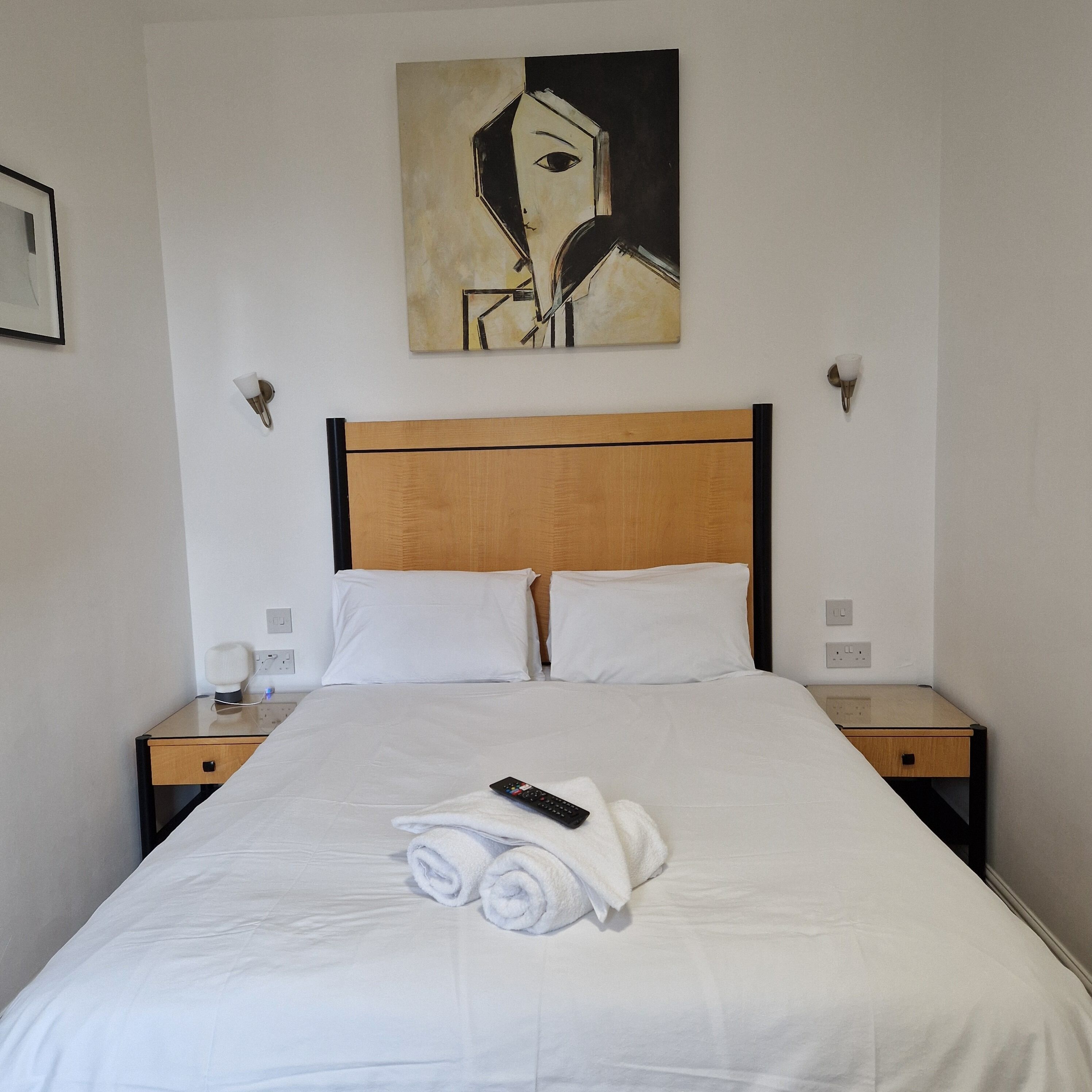 A neatly made bed with white linens, a remote control, and rolled towels on the bed.