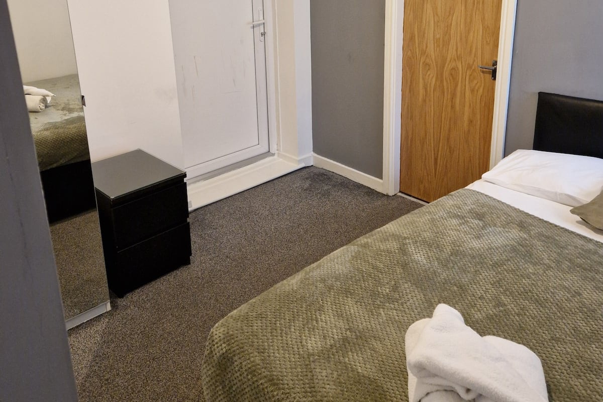 A bedroom with a bed, a wooden door, a white closet, and a small black dresser.
