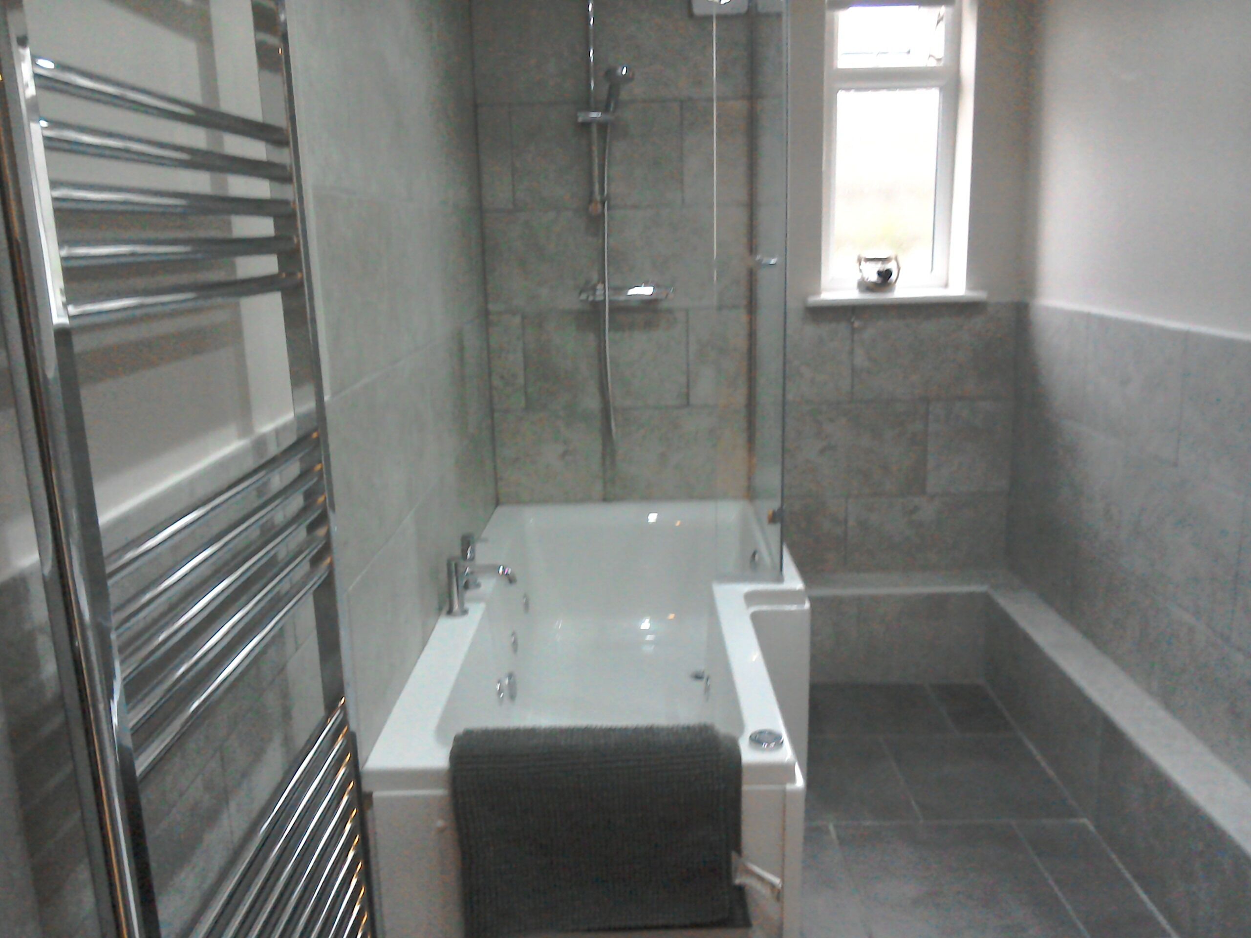 A modern bathroom with a glass-enclosed shower, a white bathtub, and a towel rack.