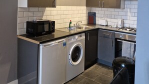 A compact kitchen with a washing machine, microwave, and a gas stove. - The Dorchester Hotel (Hull)