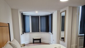 A hotel room with a large bed, a small bench, a mirror, and a window with curtains. - The Dorchester Hotel (Hull)