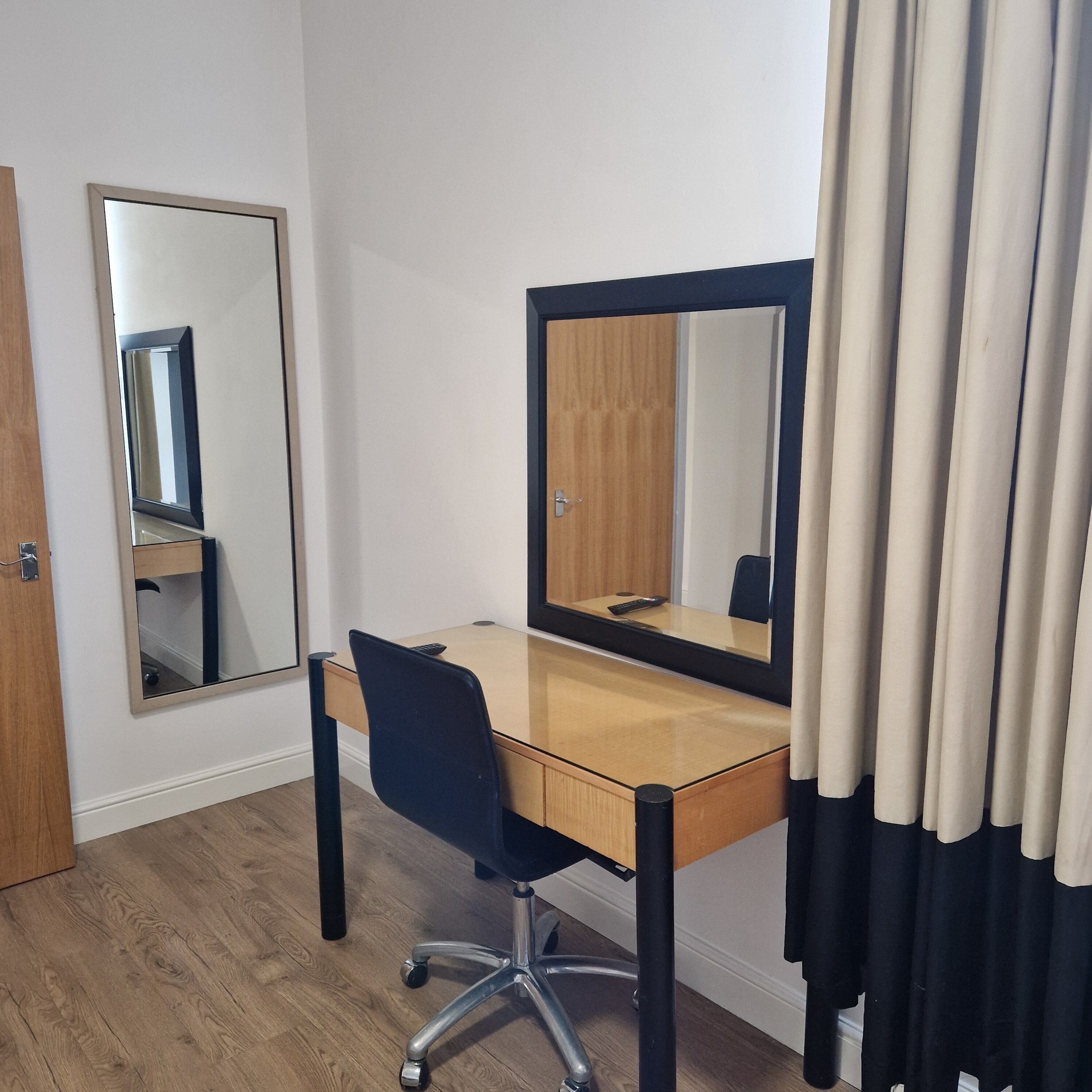 A room with a wooden desk, a chair, a mirror, and a door.
