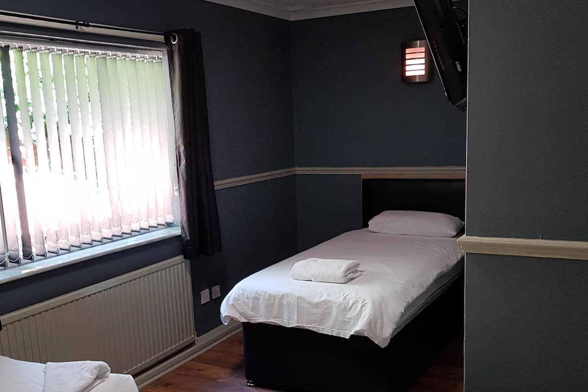 A room with a bed, a window with curtains, a radiator, and a wall-mounted light.
