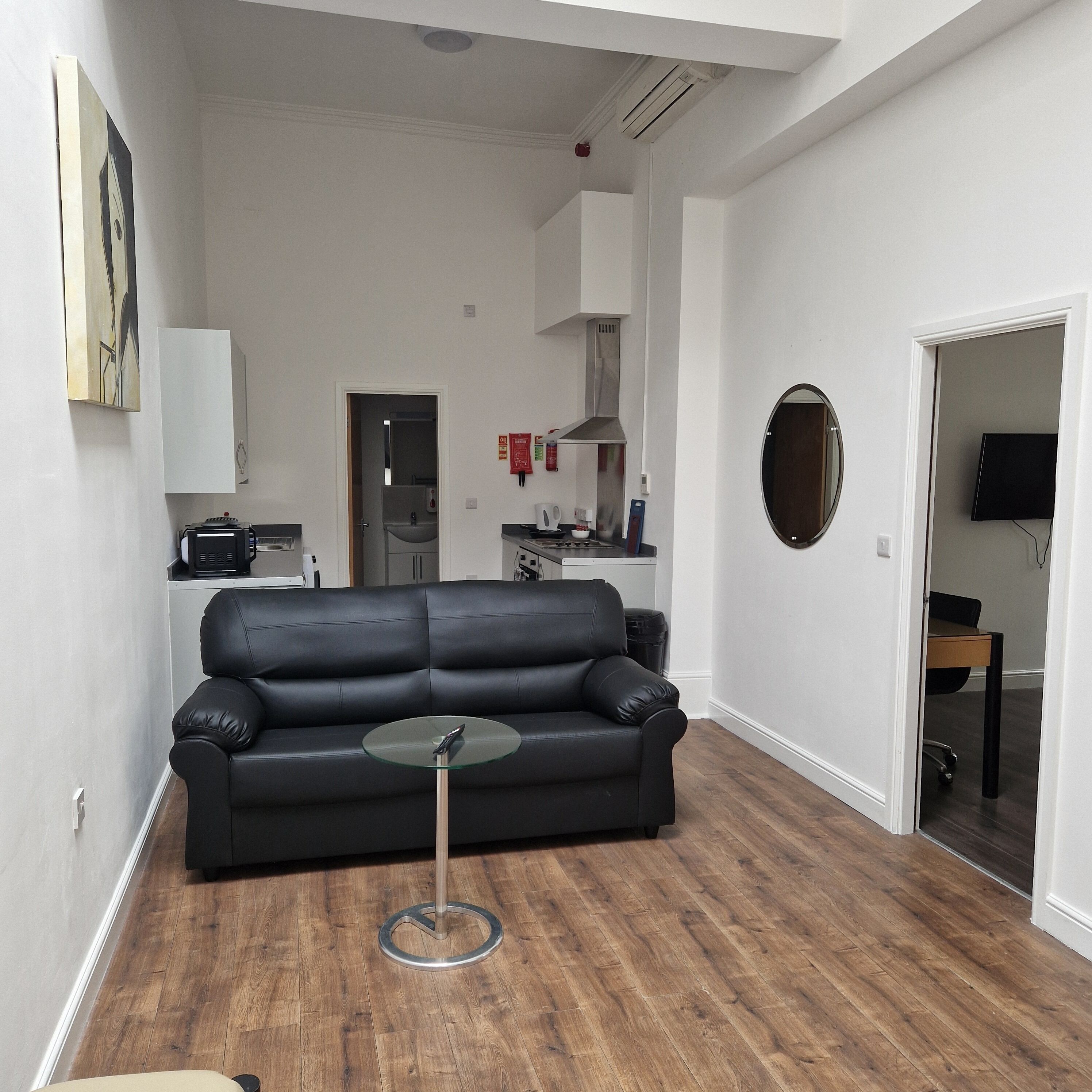 Una sala de estar moderna con un sofá de cuero negro, una mesa de centro de vidrio y piso de madera.