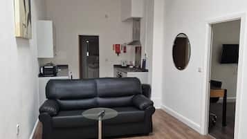 Una sala de estar moderna con un sofá de cuero negro, una mesa de centro de vidrio y piso de madera.