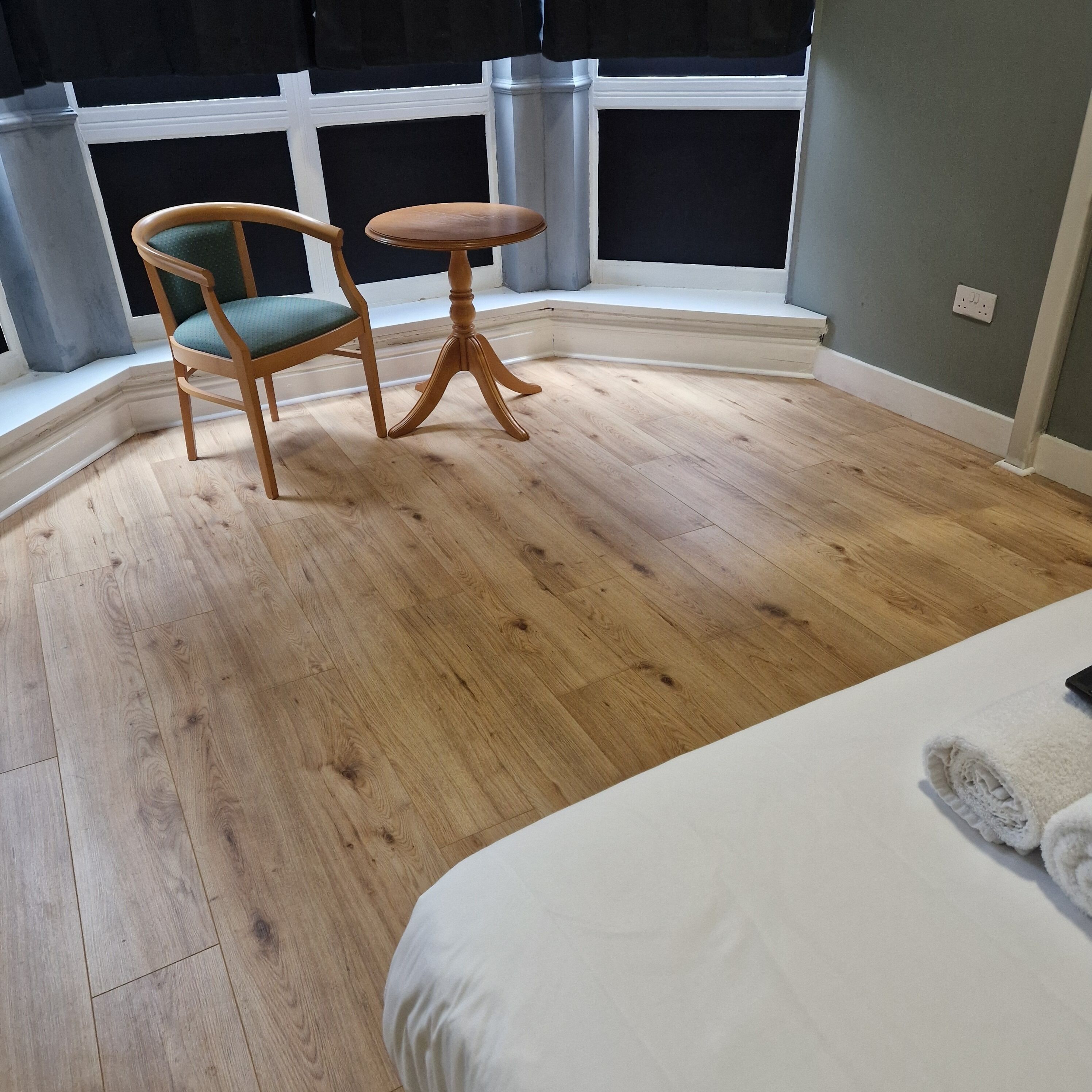 Une pièce comprenant un lit, une chaise, une petite table et une fenêtre avec des rideaux.