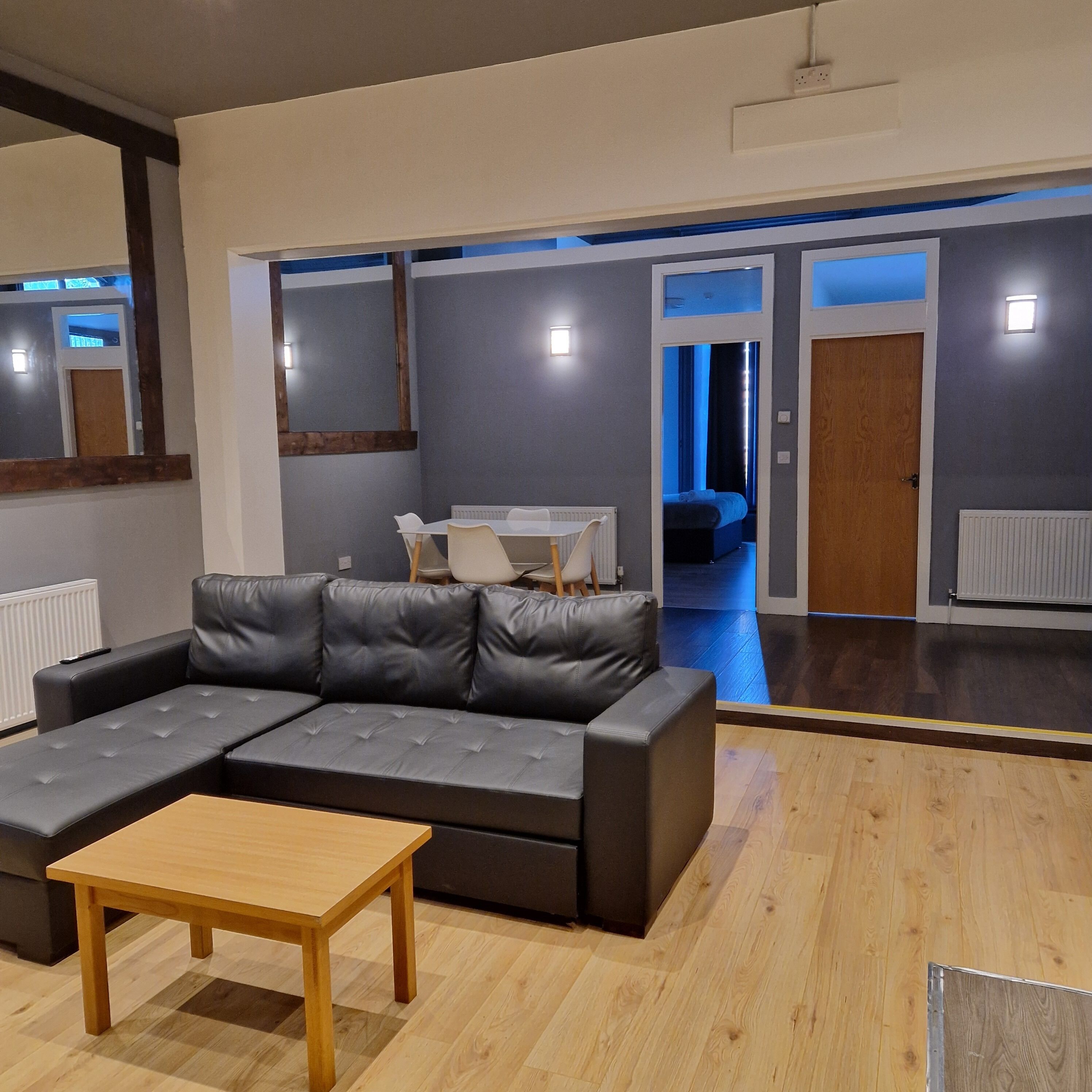 A modern living room with a sectional sofa, a wooden coffee table, and a view into a bedroom through an open door.