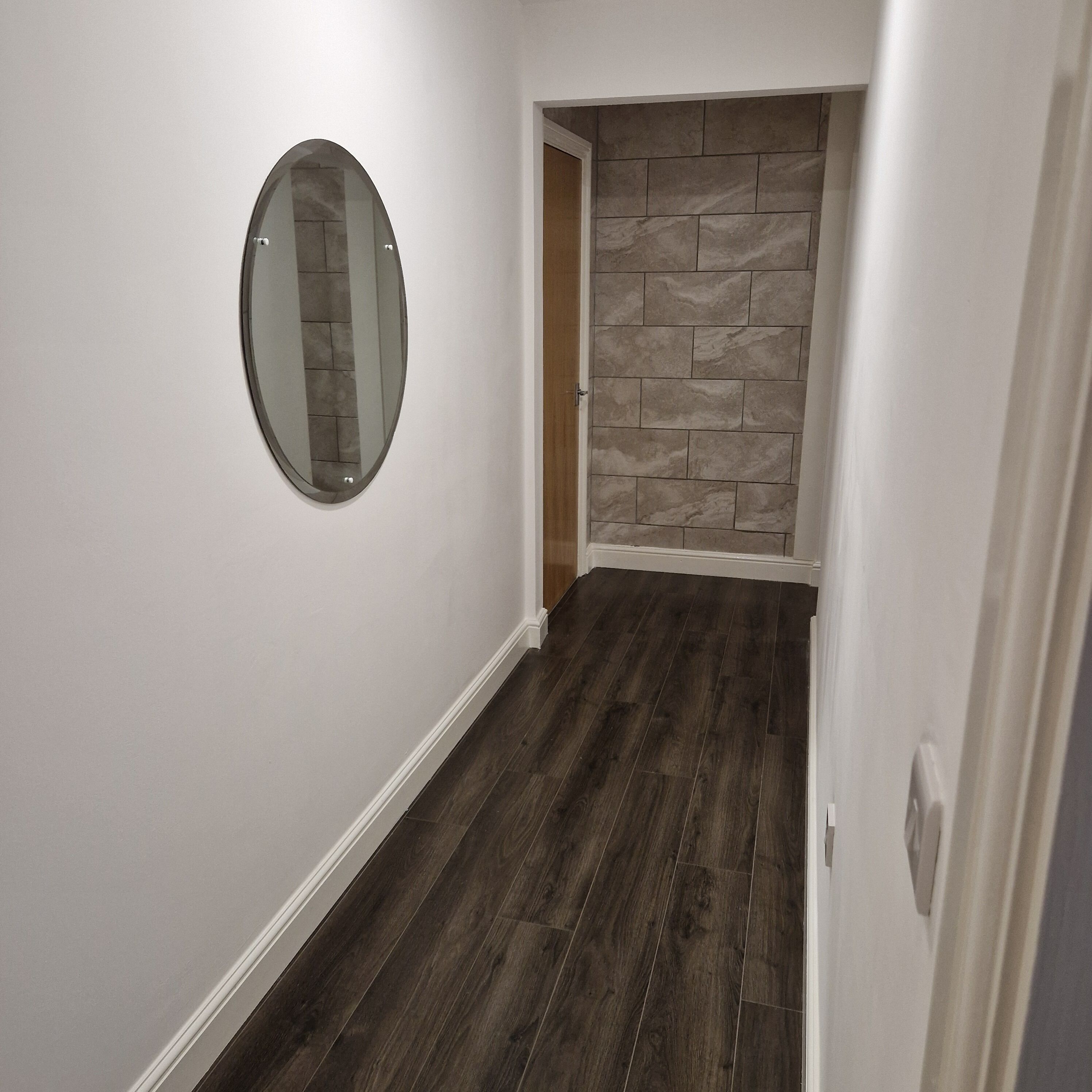 Ein Flur mit Holzboden, weißer Wand und Steinwand.