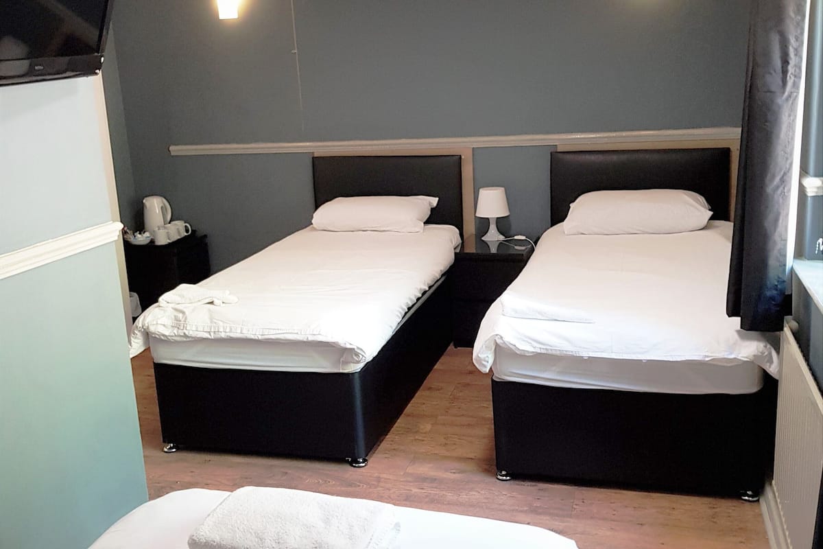 A hotel room with two single beds, a small table with a lamp, and a TV mounted on the wall.