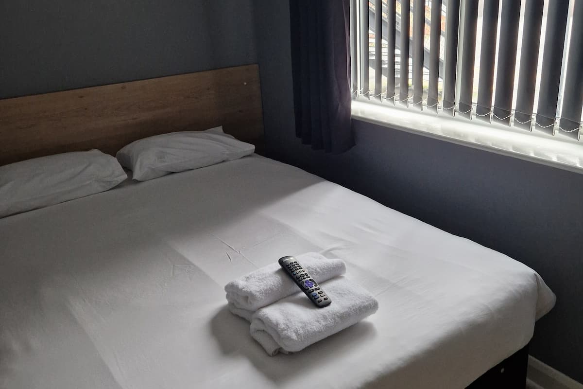 A neatly made bed with a remote control and a folded towel on the bed.