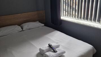 Een net opgemaakt bed met een afstandsbediening en een opgevouwen handdoek.