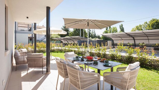 A patio with outdoor furniture and a table set for dining, surrounded by greenery and a clear sky. - Apartment Petra with Pool (Lazise)