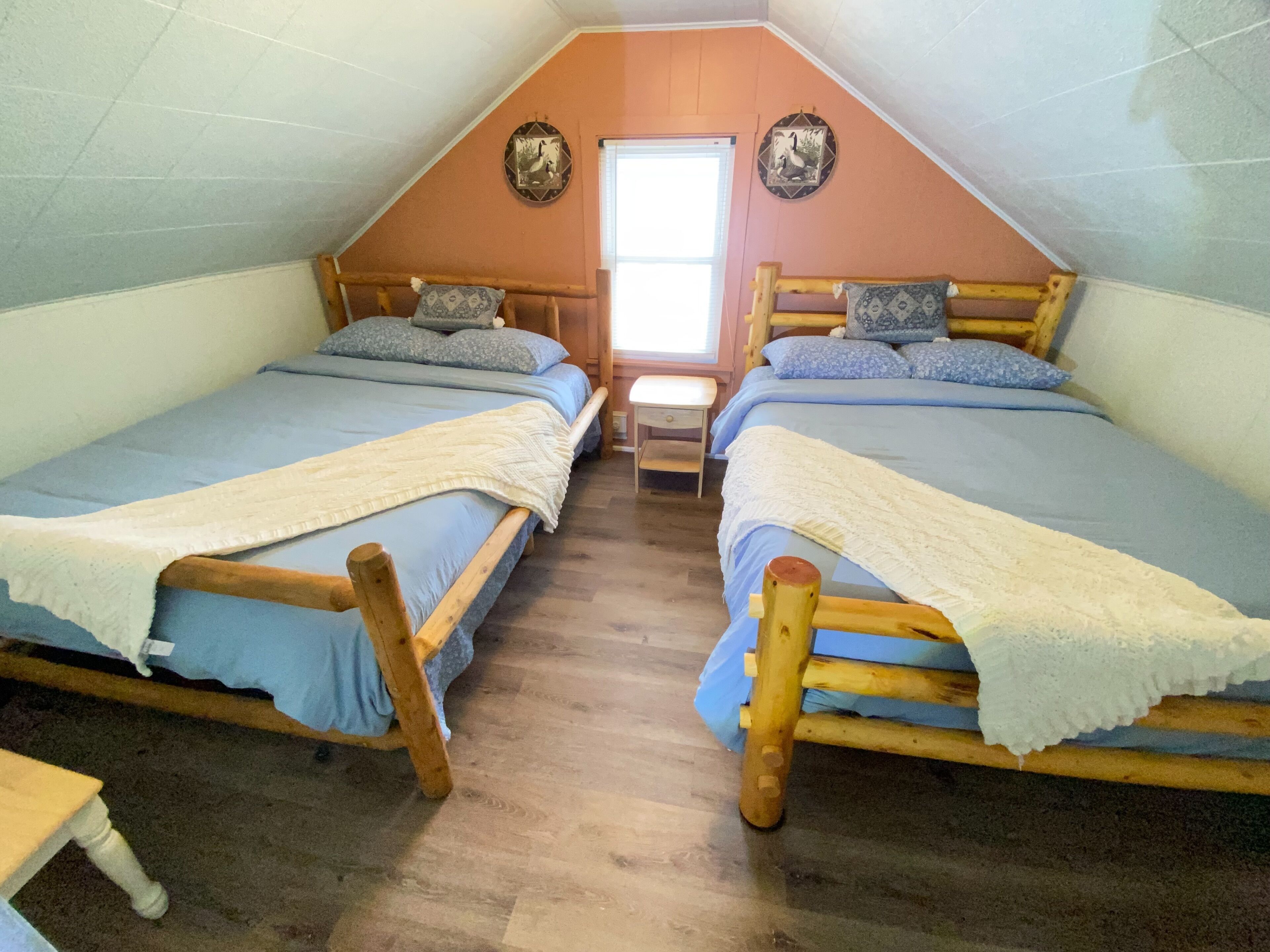 A dormitory room with two wooden bunk beds, a small table, and a window.