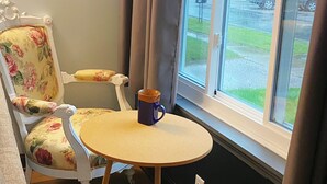 Een kamer met een ronde tafel, een fauteuil met bloemenmotief en uitzicht op de straat door een raam.