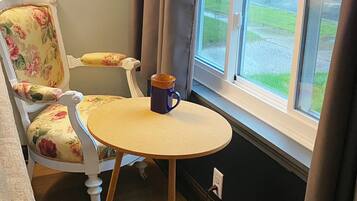 Ett rum med ett runt bord, en blommönstrad fåtölj och utsikt över gatan genom ett fönster.