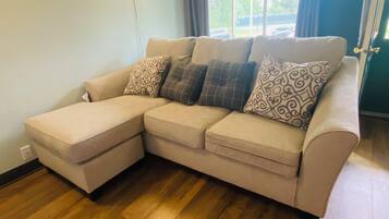 A beige sectional sofa with patterned cushions, a wall-mounted light, and a view of the outdoors through a window.